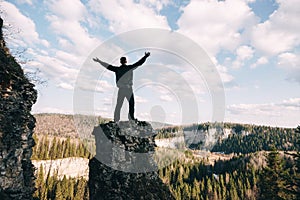 Young man standing with raised hands on top of a mountain and enjoying valley view