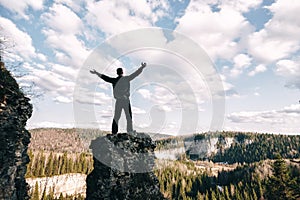 Young man standing with raised hands on top of a mountain and enjoying valley view