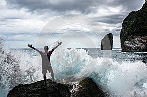 Young man standing on the rock with the sea waves breaking in frront