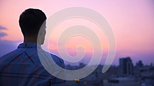 Young man standing on roof of building alone and meditating, enjoying freedom