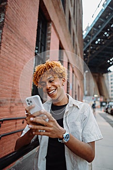 A young man is standing on a sidewalk looking at his cell phone