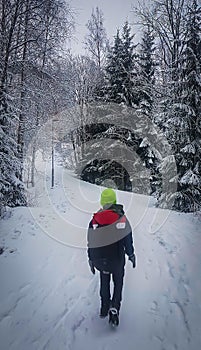 Young man standing among snowy trees in winter forest and enjoying first snow. Wearing hat and bagpack on travel