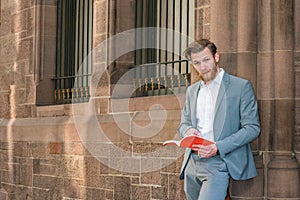Young man standing on street in New York City, reading red book