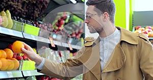 Young man standing in supermarket and choosing oranges. Stylish man looking at fruits while shopping.