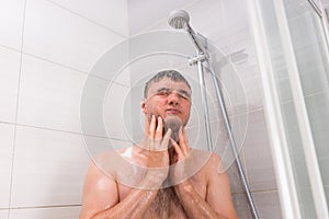 Young man standing under flowing water in shower cabin