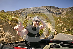 Young Man Standing Up Through Sun Roof Car On Road Trip Through Countryside