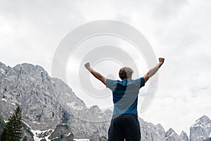 Young man standing victorious with his arms raised high surrounded with mountains