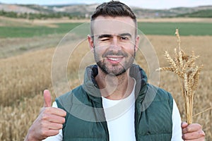 Young man standing in wheat field and showing thumb up while winking and smiling