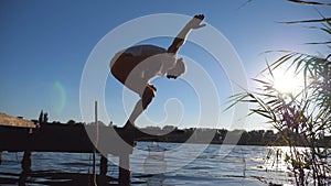 Young man standing at yoga pose on the edge of a wooden jetty at lake. Sporty guy doing exercise outdoor. Summer