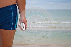Young man stands against the sea shore beach sand waves water horizon holds in hand a seashell