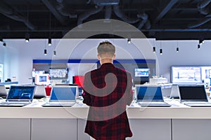 young man stands behind his laptop at the electronics store. A young man chooses a laptop in the store