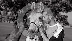 Young man stands and holds white horse by the bridle