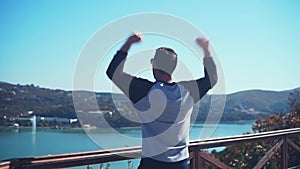 A young man stands, looking from the observation deck and bouncing up, raising his hands in awe of happiness.