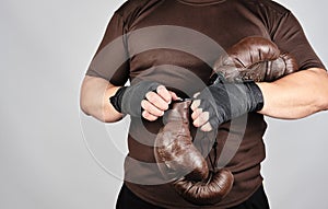 young man stands and puts on his hands very old vintage brown boxing gloves