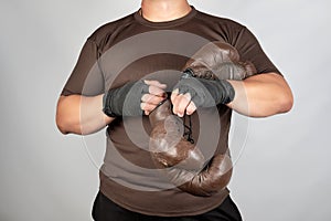 young man stands and puts on his hands very old vintage brown boxing gloves