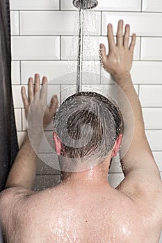 A young man stands in the shower under running water and leans h