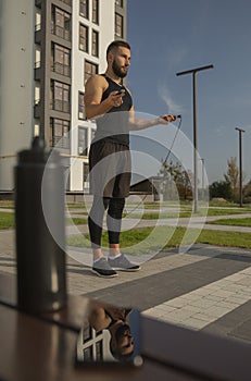 A young man stands with a skipping rope. Its display is in the smartphone.