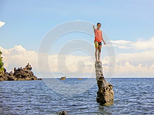 Young man stands on a stone column in the sea. Cliff protruding from the sea. The rocky coast of the Balinese sea.Beautiful nature