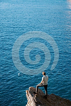 Young man stands on a stone ledge above the sea and looks into the distance. Back view