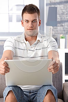 Young man staring at laptop screen horrified