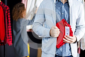 Young man is stealing red jeans in store