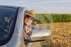 Young man in straw hat driving truck and looking at his plantations.