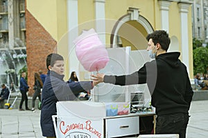 Young man street sweets seller selling cotton candy to the teen boy.