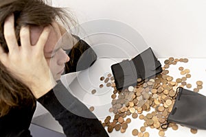 a young man with stressful emotions holds his head with his hands over a mountain of small coins with a wallet, a piggy bank bag.