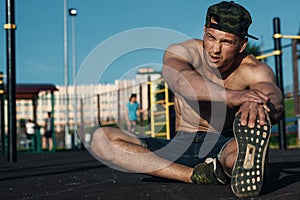 A young man stretches out on a sports field, an athlete, training outdoors in the city. copy space