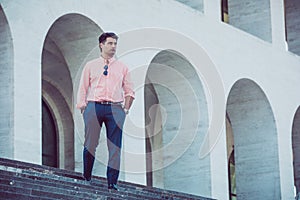 Young man with striped shirt and pants outdoors with hands in pockets. Walking up the stairs with a building behind it. Sunglasses