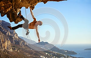 Young man struggling to climb ledge on cliff