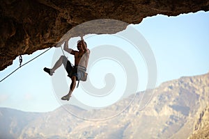 Young man struggling to climb ledge on natural cliff