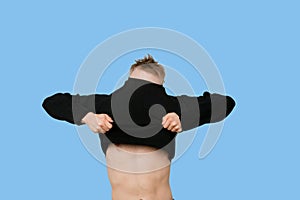 Young man struggling to pull down t-shirt over blue background