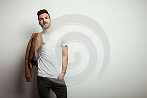 Young man with stubble in blank t-shirt and jacket, empty wall in studio background