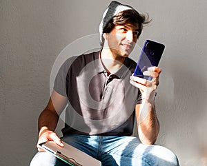 Young man student sitting holding a folder and sending a voice message with a phone over white background