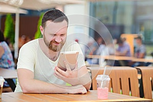 Young man student using a tablet computer in a cafe with a cool drink in the city.
