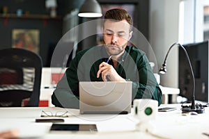 Young man studying with laptop computer on white desk.