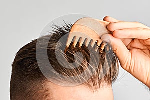 Young man styling his hair with a wooden comb. Hair styling at home. Advertising concept of shampoo for healthy hair and