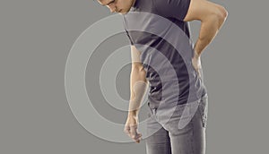 Young man suffering from back pain due to large physical exertion isolated on gray background.