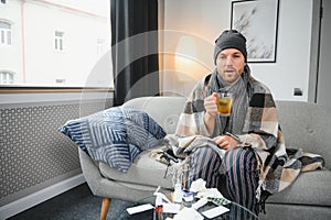 Young man suffering from a common cold and flu or allergy sit at home wrapped in blanket and wipe his nose with tissues