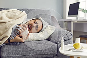 Young man suffering from flu or bad cold lying on sofa and sneezing in paper tissue