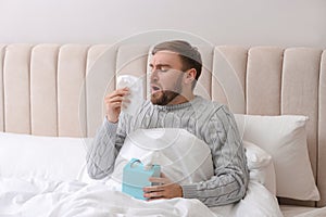 Young man suffering from runny nose in bed indoors