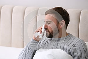 Young man suffering from runny nose in bed indoors
