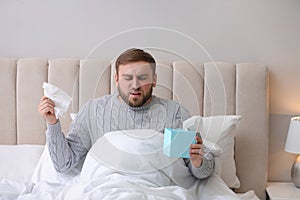 Young man suffering from runny nose in bed indoors