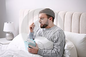 Young man suffering from runny nose in bed indoors