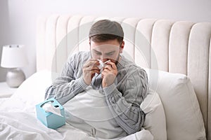 Young man suffering from runny nose in bed indoors