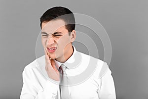 Young man suffering from toothache on grey background