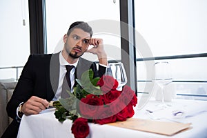 young man in suit with bouquet of red roses waiting for girlfriend
