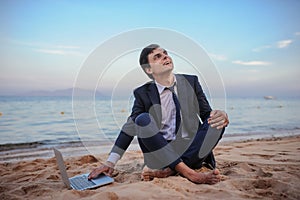 young man in suit with laptop sitting on the beach working on the seaside