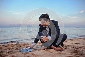 young man in suit with laptop sitting on the beach working on the seaside